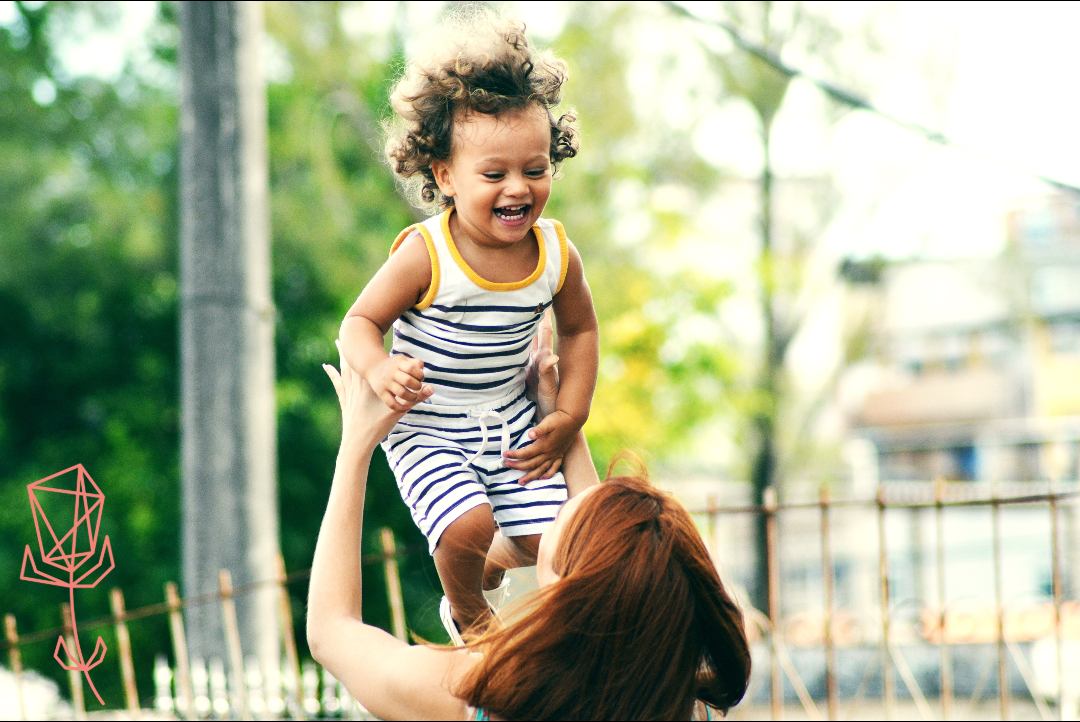 Mom throwing laughing baby up in the air, outdoors in a park
